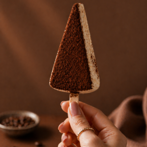 Handcrafted Tiramisu Cheesecake Cakesicle coated in white chocolate with cocoa powder by Kek & Crust Malaysia.